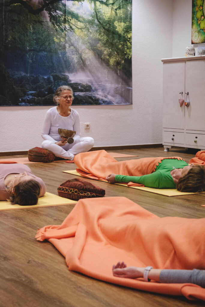 Yoga-Lehrerin Angela Kiesewetter-Lorenz im Schneidersitz, Kursteilnehmerinnen liegend