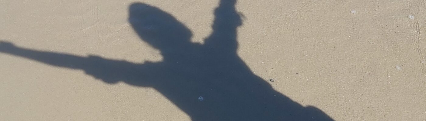 Schatten mit erhobenen Armen auf Sand am Meer
